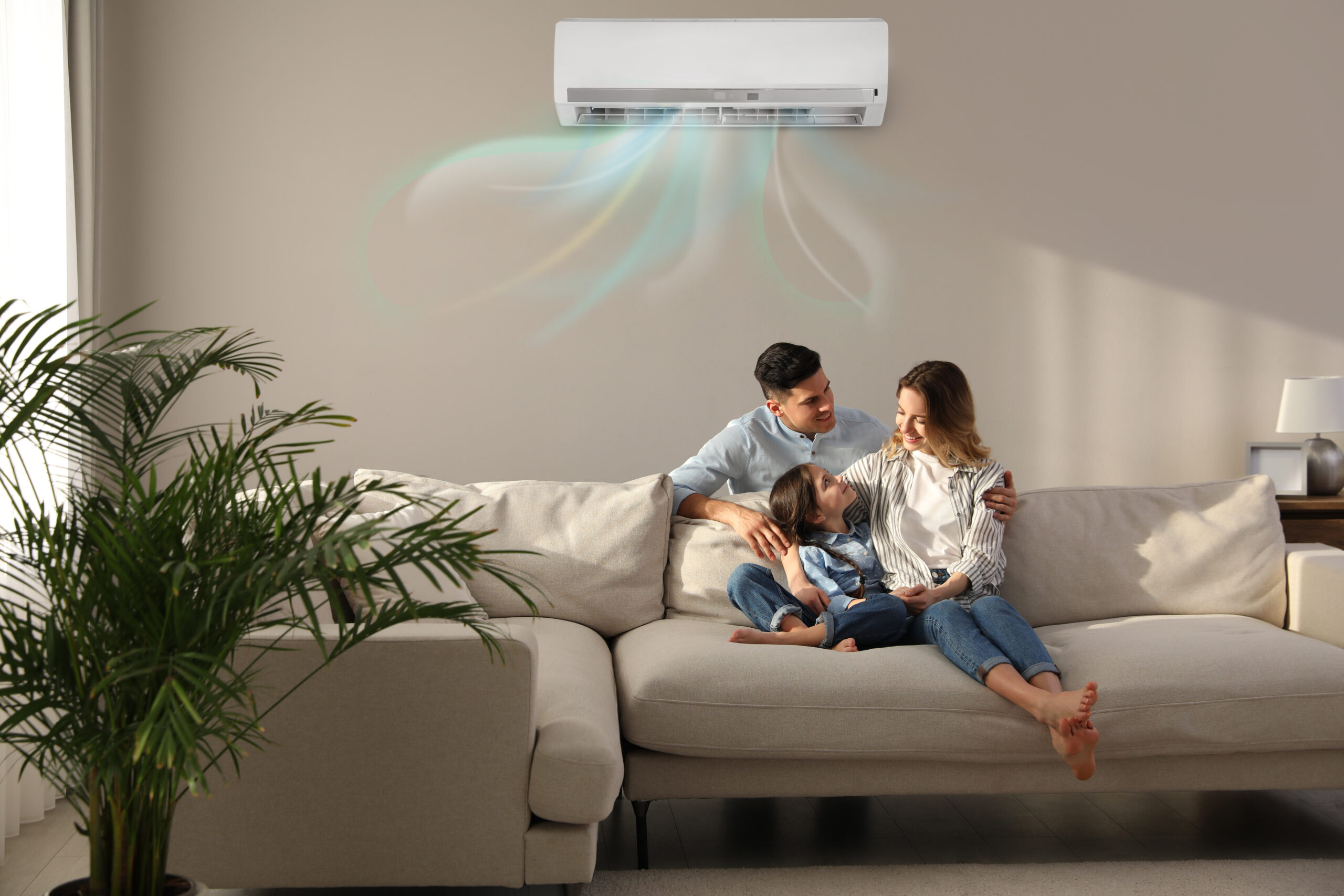 A family enjoys a comfortable snuggle on the sofa under a ductless HVAC unit keeping the room at a nice temperature.